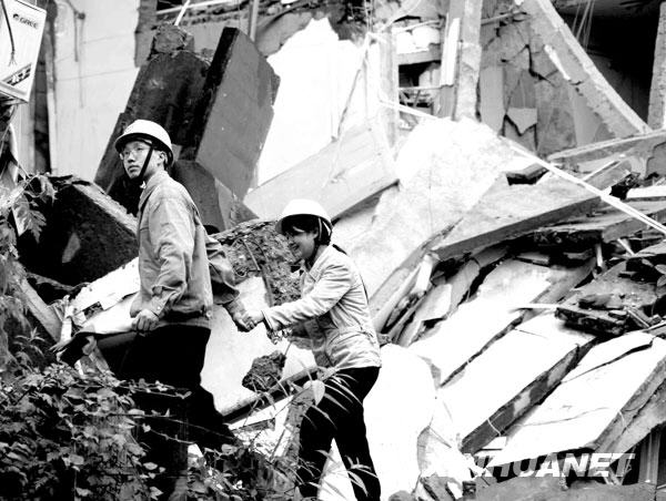 2008年5月13日，东方汽轮机厂领导将一位向废墟里喊话的女青年（右）从十分危险的废墟旁带走。东方汽轮机厂是四川德阳一大型国有企业，地震发生后，有近千名员工、家属遇难或失踪。这位女青年的弟弟所在的科研车间中有多名科研人员被掩埋，眼看着亲人被埋在废墟中无法施救，勇敢的姐姐走近十分危险的废墟，哭喊着鼓励弟弟坚强地活下来。